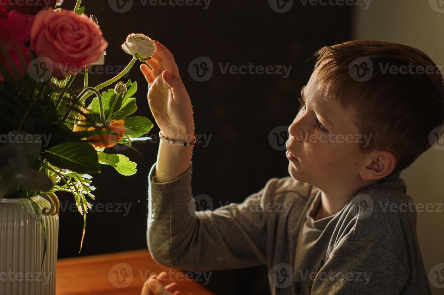 The golden glow of sunrise frames a boys silhouette as he touches a floral arrangement. photo