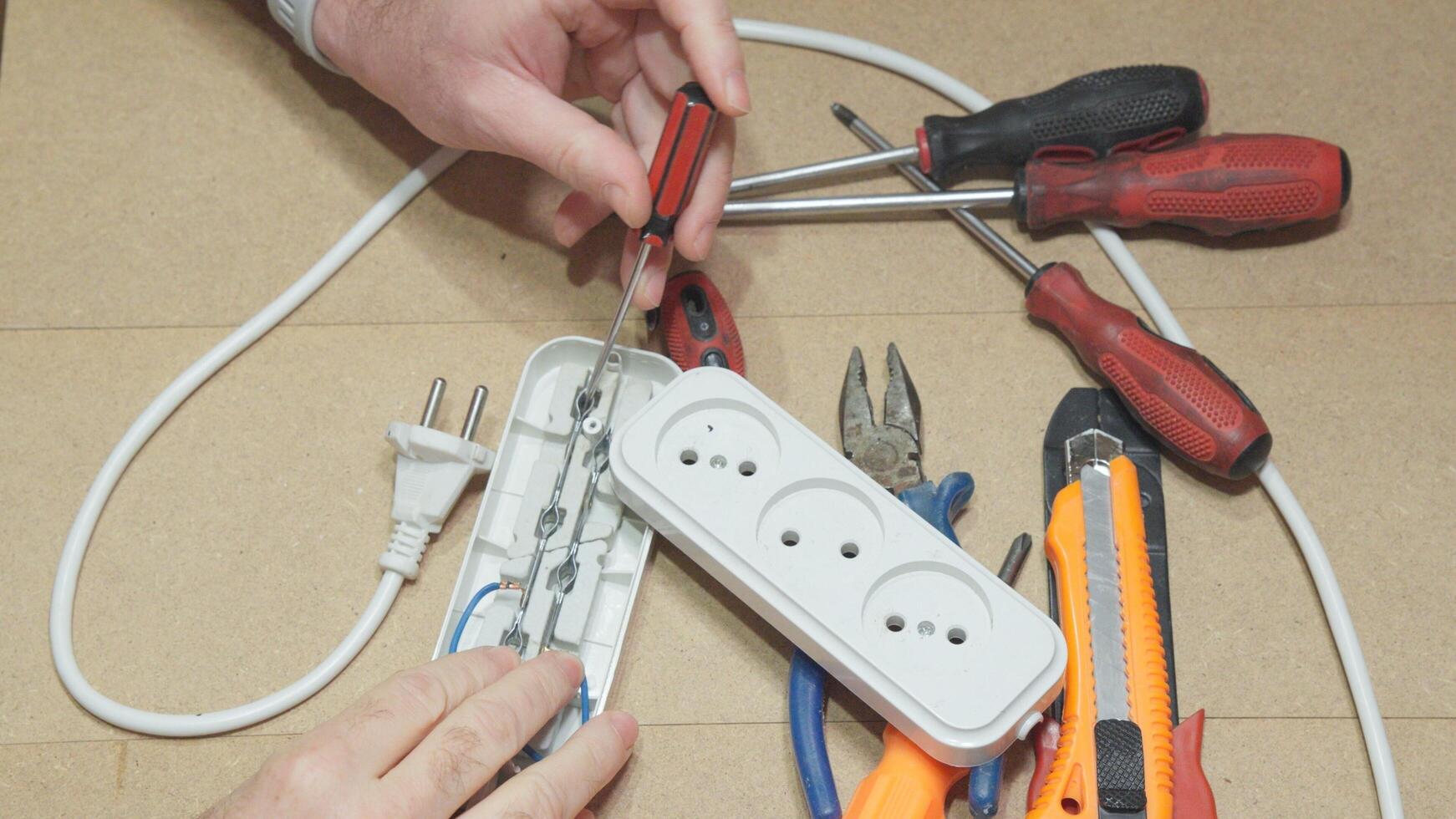 A hand holds a screwdriver while repairing an extension cord with an open cover. photo