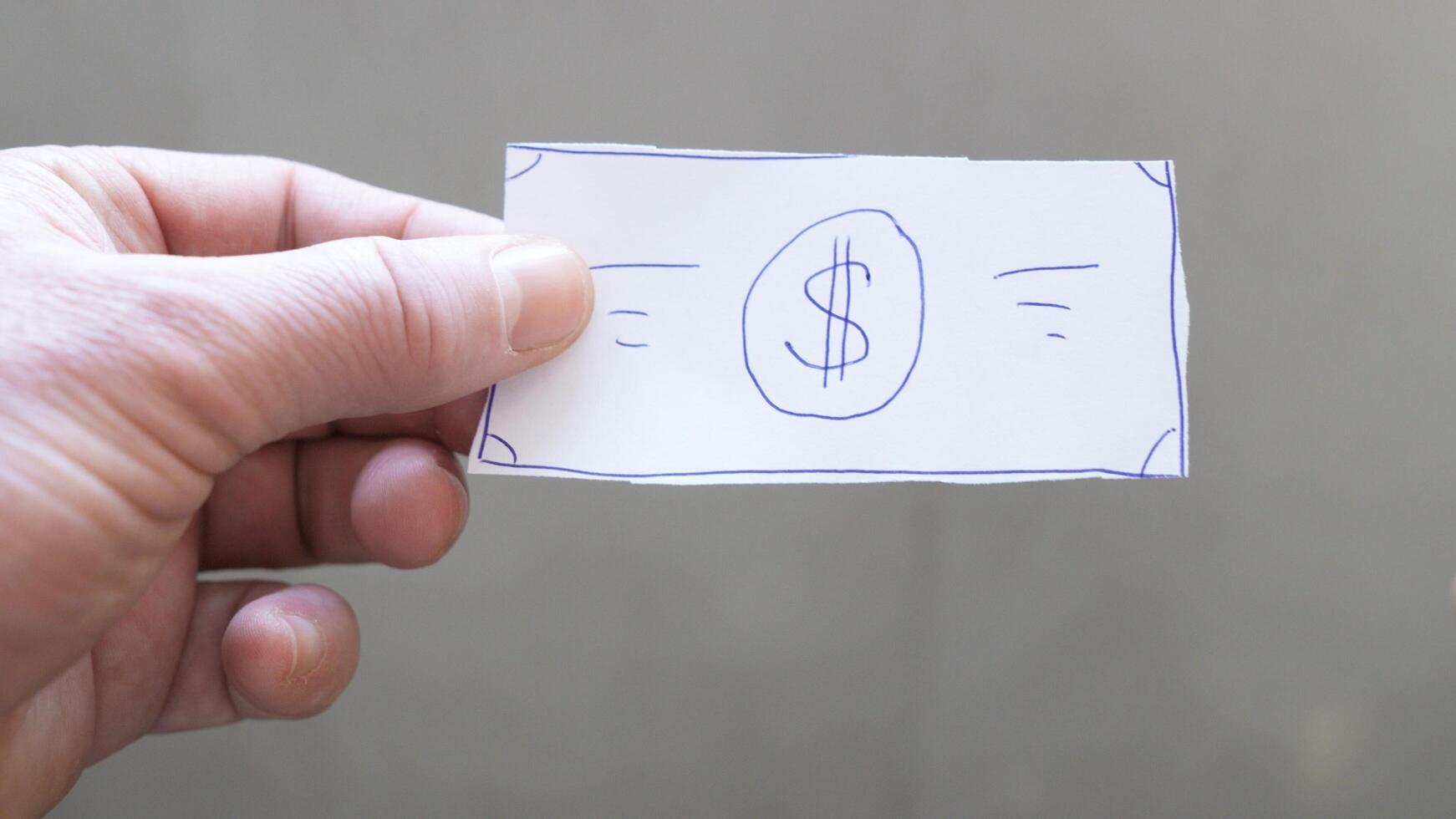 A piece of paper resembling a dollar bill, with a dollar sign drawn in the center, is being held in hand. This item may be used for illustration or as a humorous element. photo