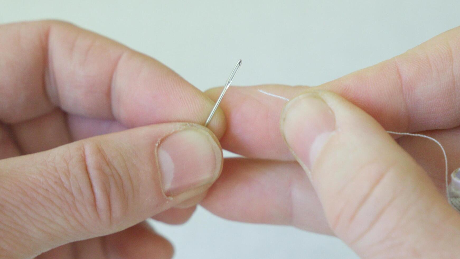 A hand holds a needle and thread, preparing them for sewing. photo