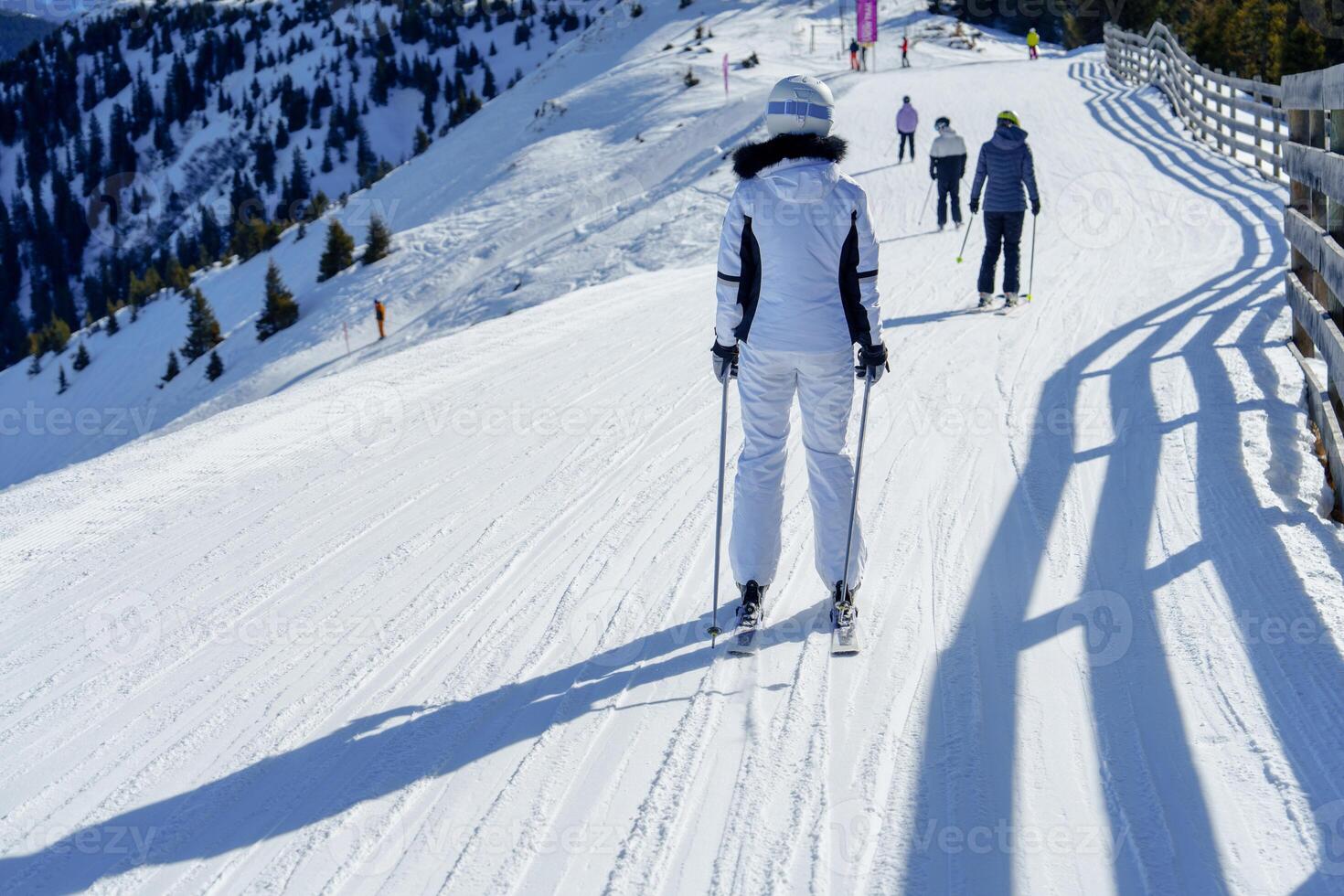A female skier in a white protective suit gracefully descends a snowy slope in the breathtaking Austria, Alps, showcasing the thrill of winter sports in this stunning mountain landscape. photo