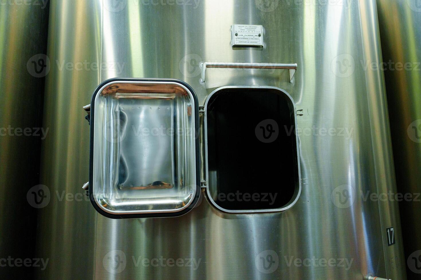 A large stainless steel tank stands prominently, its shiny surface reflecting light. An open hatch reveals a dark, mysterious interior, hinting at its industrial purpose and potential uses. photo