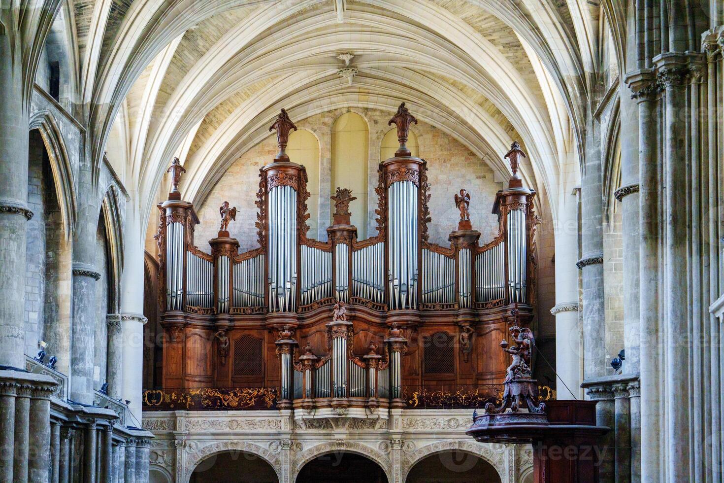 The grand organ, adorned with exquisite carvings and multiple golden pipes, stands majestically in the church, enhancing the architectural beauty of the vaulted ceiling and the overall ambiance. photo
