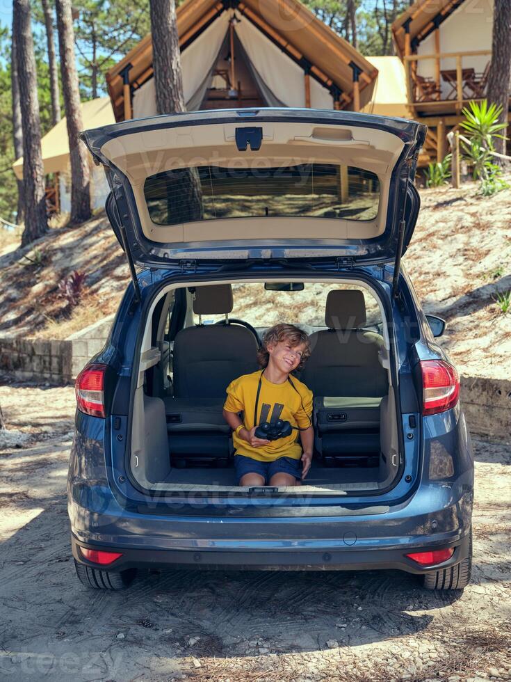Boy having fun while sitting in trunk near glamping campsite photo