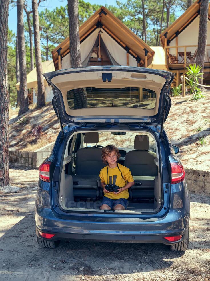 Boy sitting in car trunk and holding binoculars photo