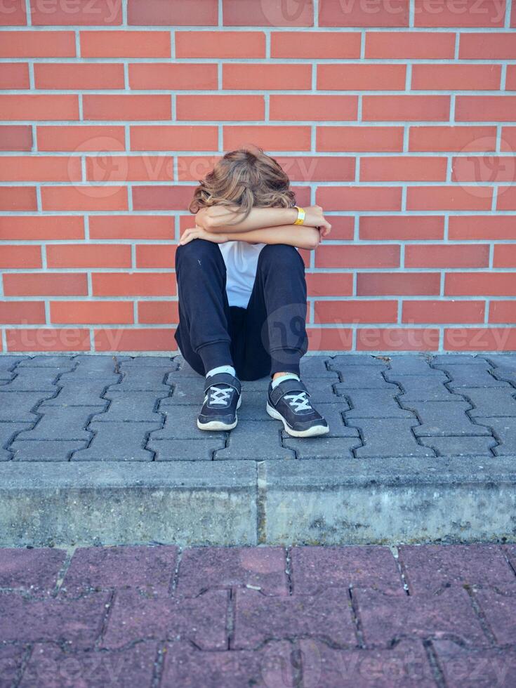 Unrecognizable boy hugging knees and sitting near brick wall photo