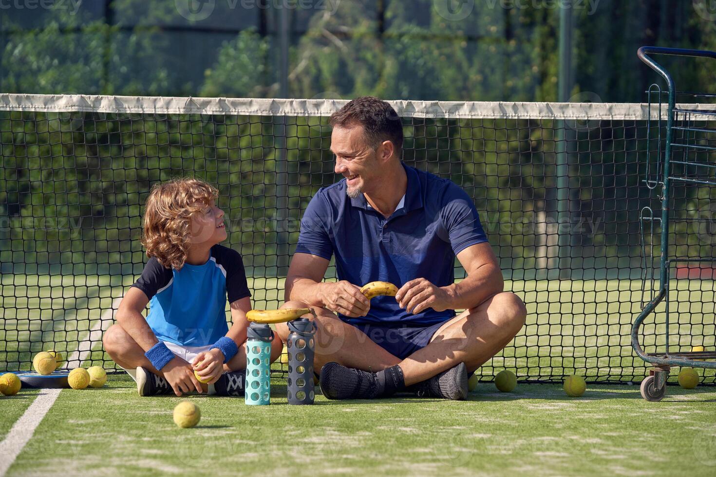 Cheerful coach with boy sitting on court photo