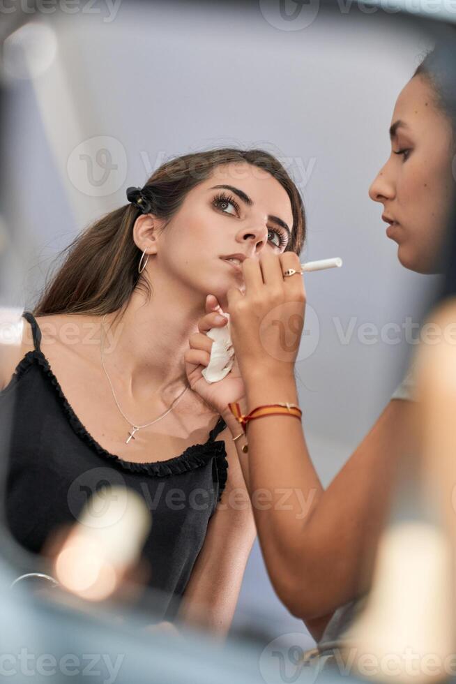 Woman applying lipstick on woman near mirror photo