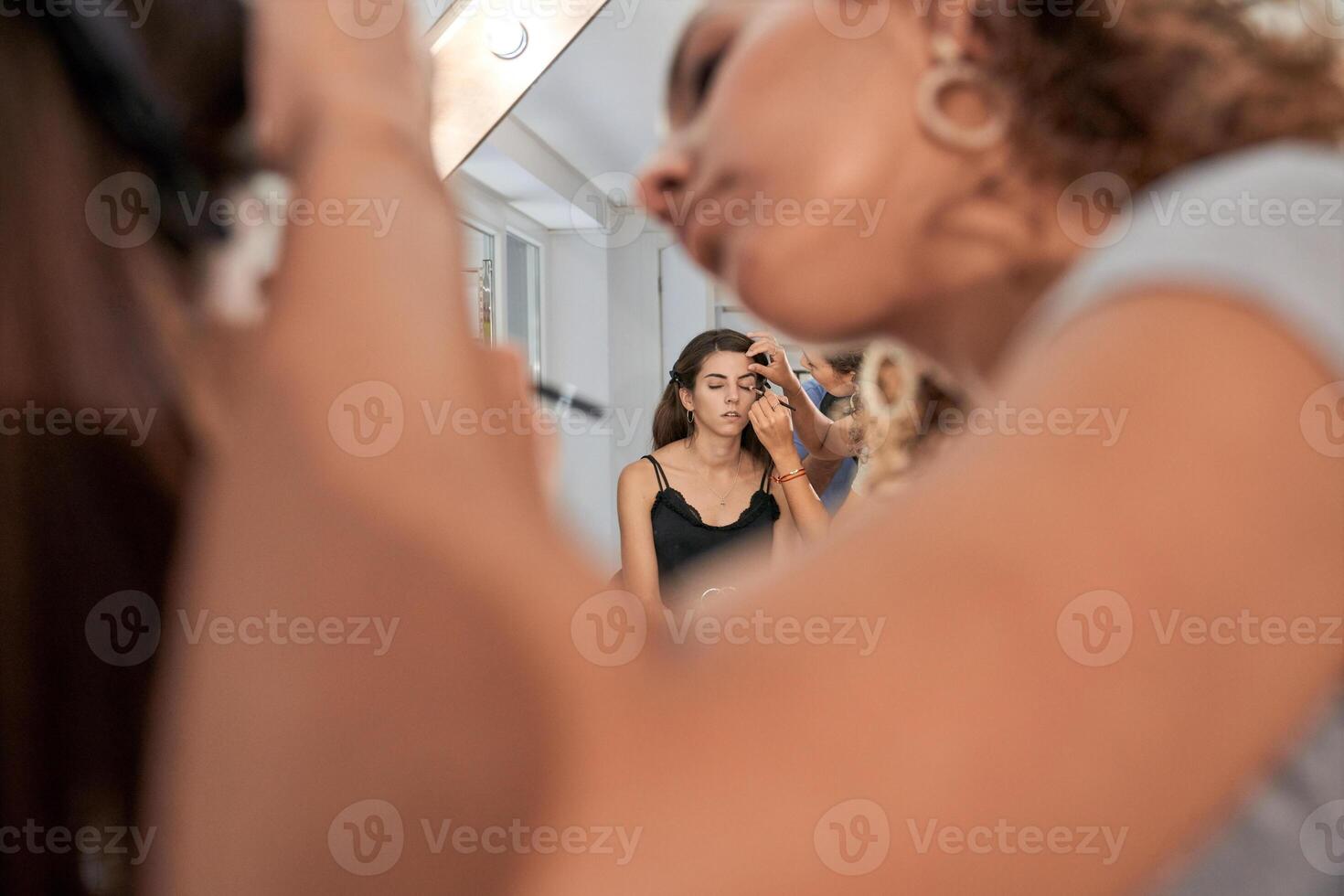 Focused woman applying eyeshadow on woman near mirror photo