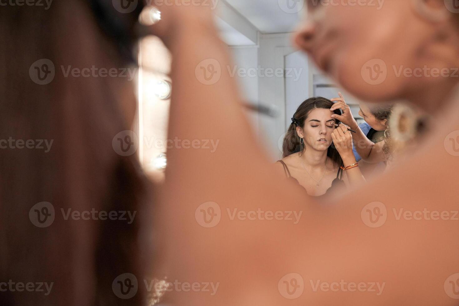 Unrecognizable visagiste applying eyeshadow on model near mirror photo