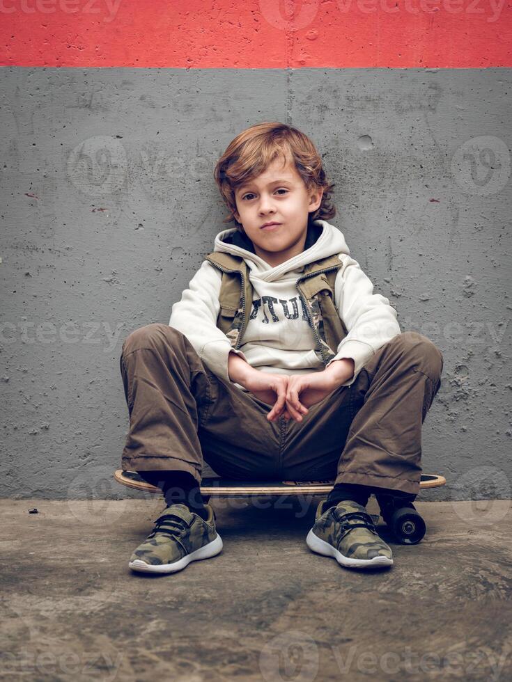 Cool child sitting on skateboard near wall photo