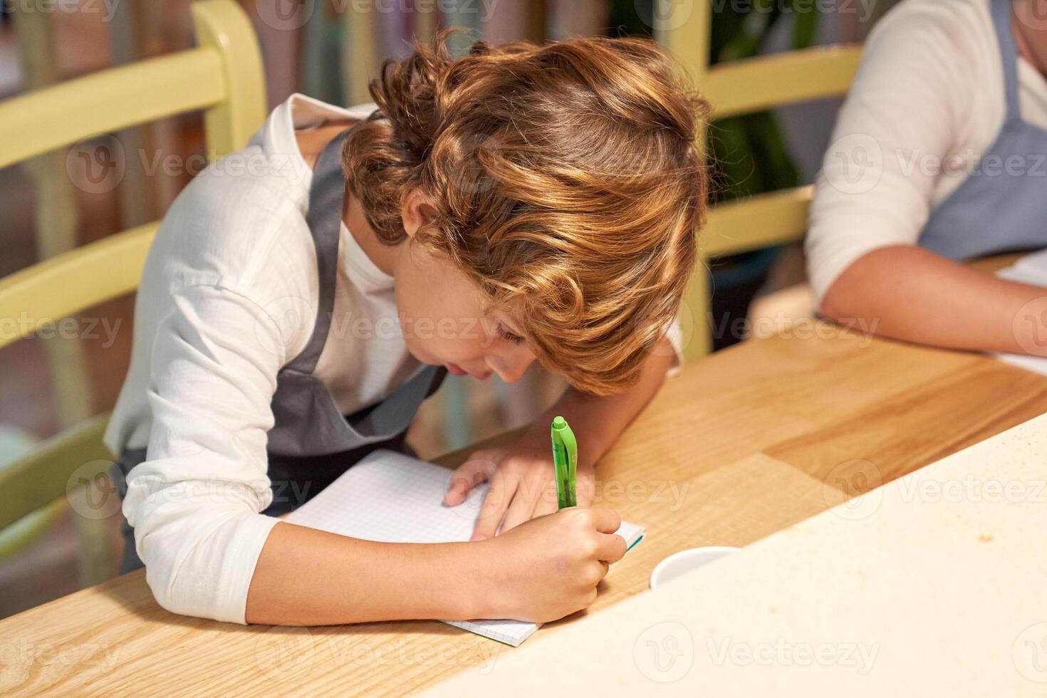 Boy writing on paper in kitchen photo