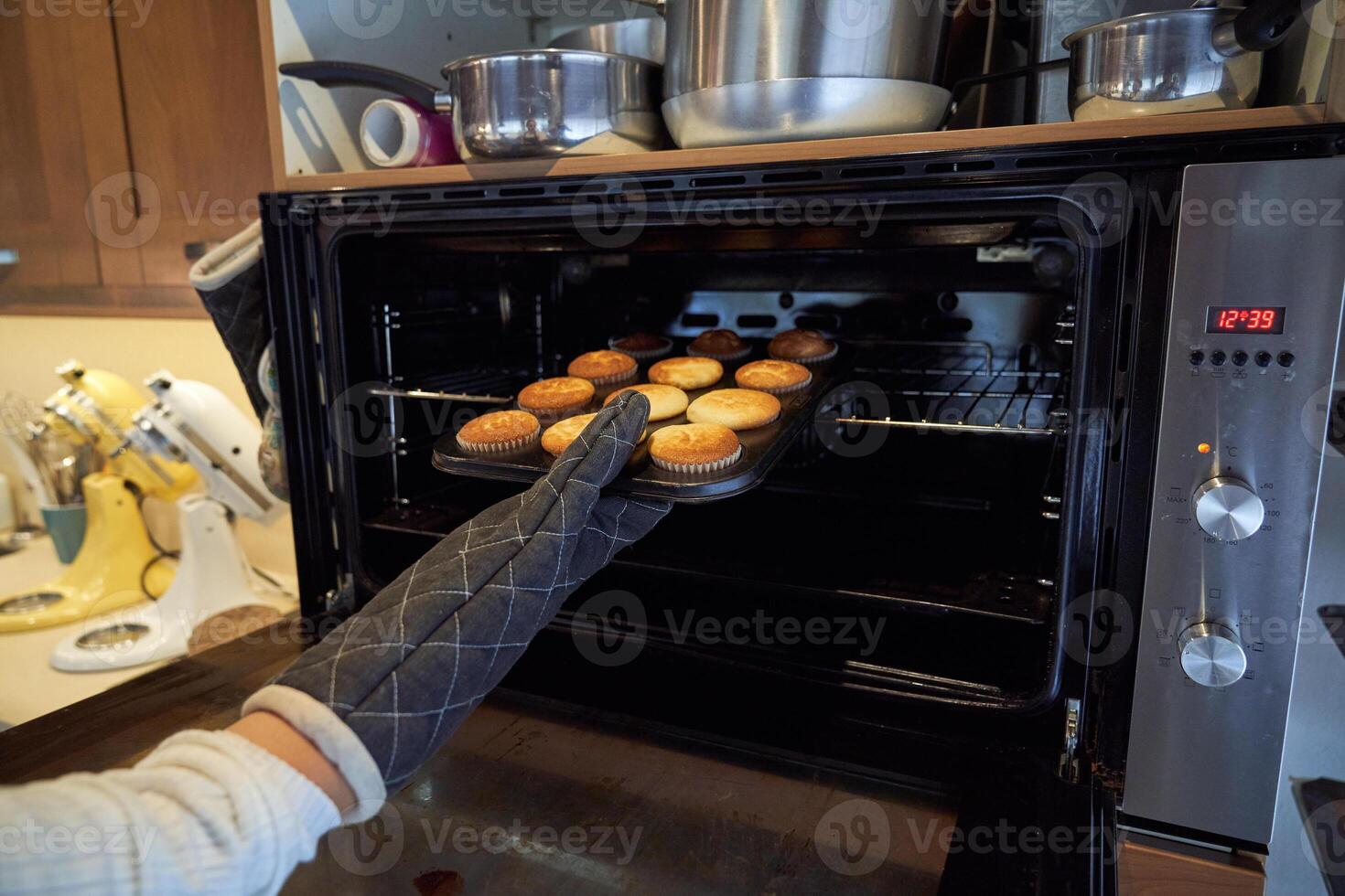 Unrecognizable person taking cupcakes from oven photo