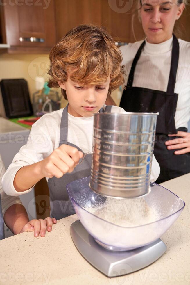 Little boy adding flour to bowl for batter photo