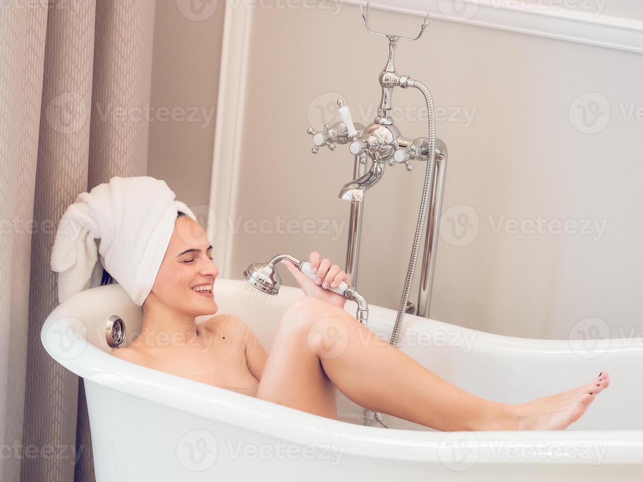 Smiling woman resting in bathtub and washing with shower photo