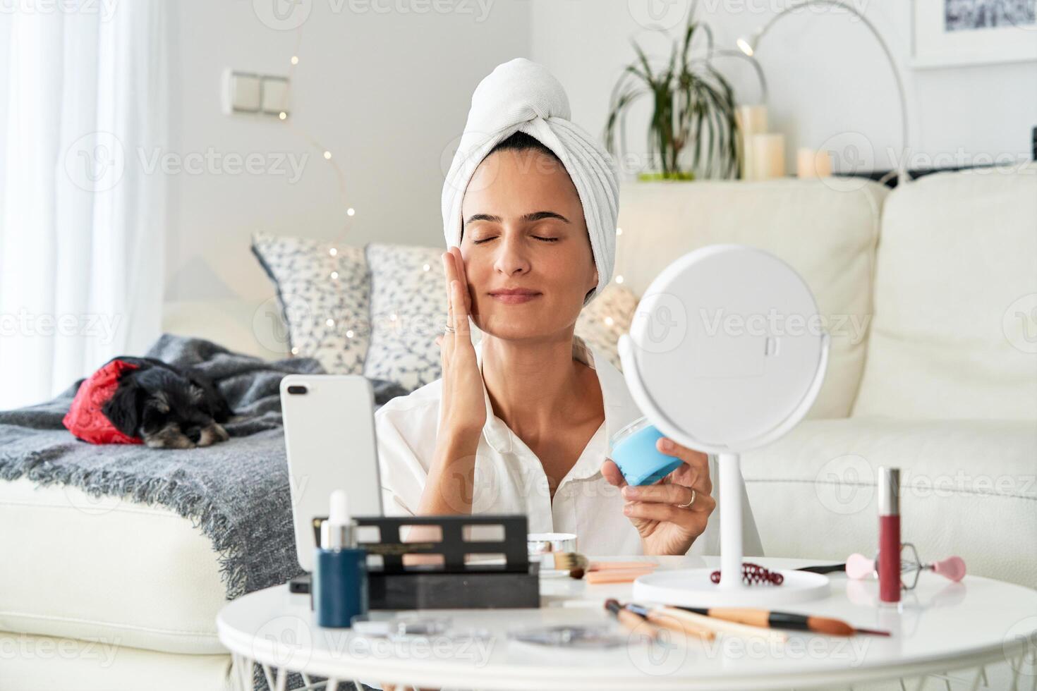 Female applying cream on face while recording on smartphon photo
