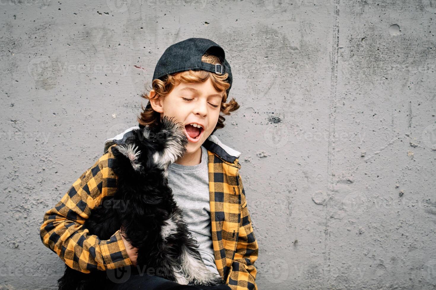 Kid holding dog and yawning against concrete wall photo