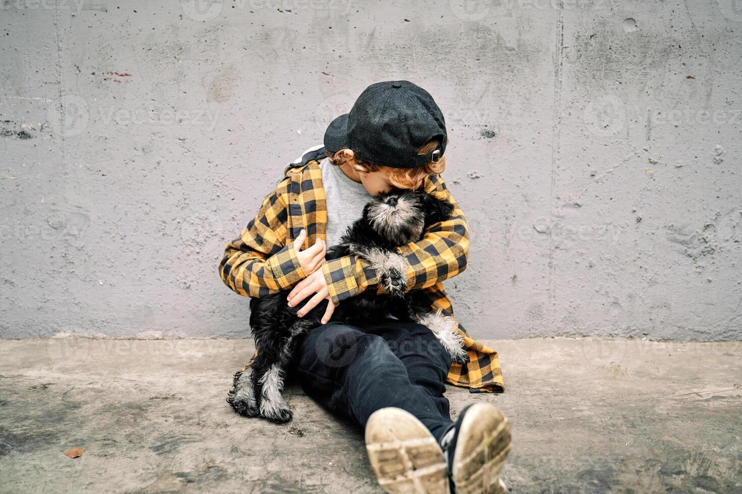 Child hugging dog while sitting near gray street wall photo