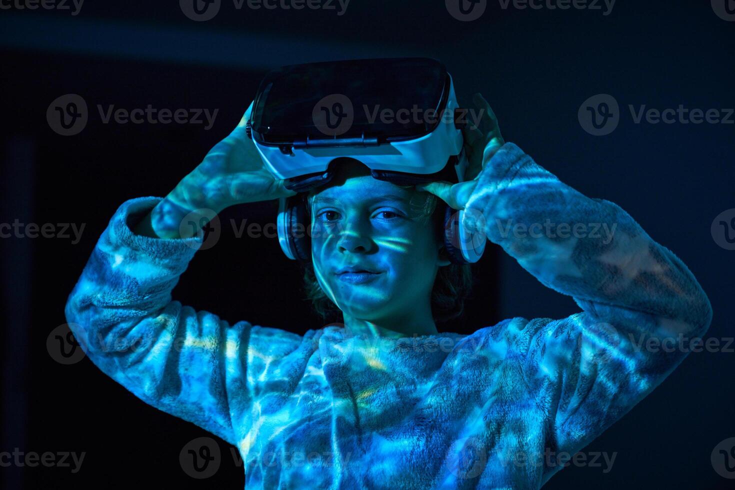 Little boy adjusting VR headset and looking at camera in darknes photo