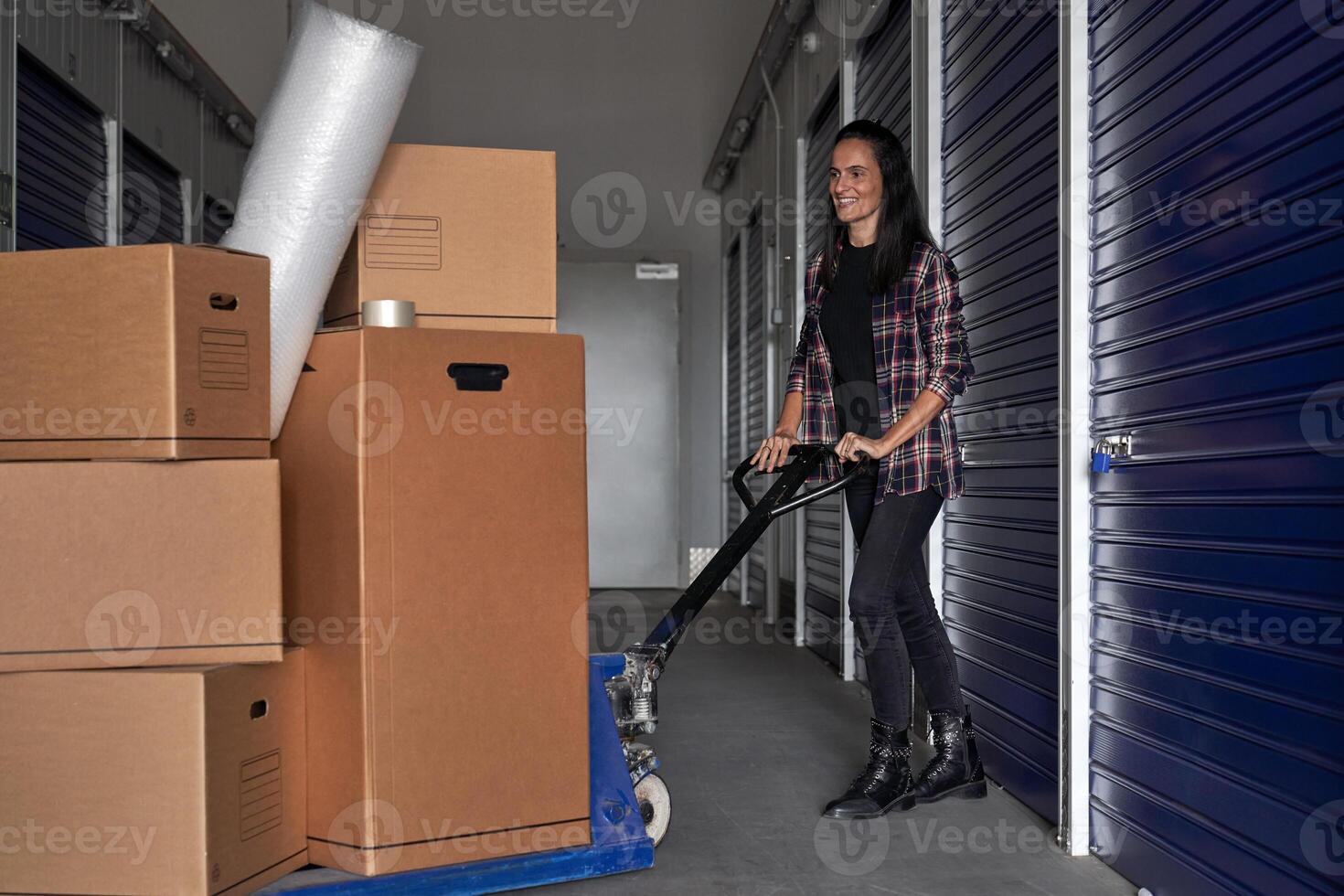 Happy woman using pallet truck to move carton boxes photo