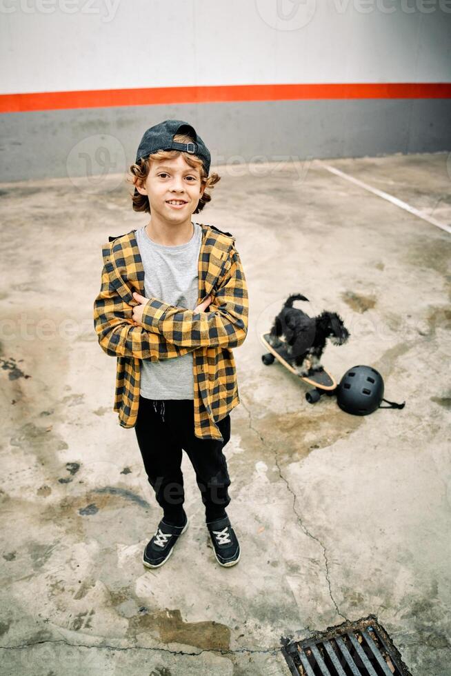 Cute boy standing on street near small dog on skateboard photo