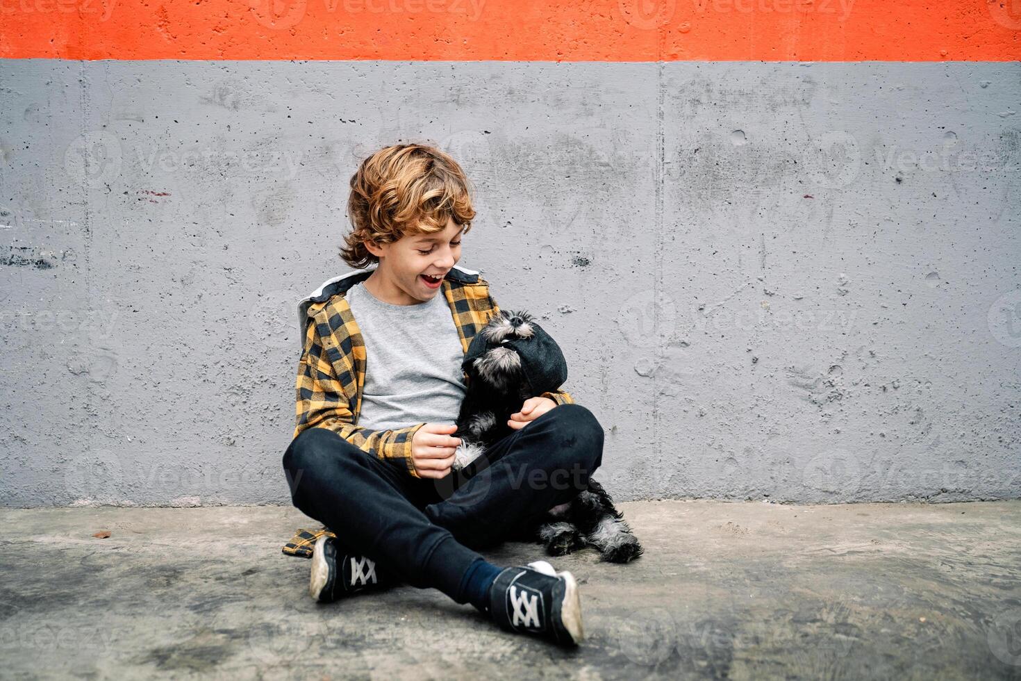 Happy kid sitting near concrete wall and looking at dog photo