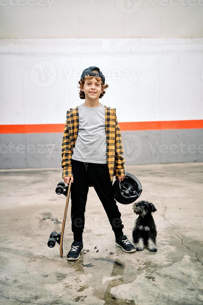Satisfied kid with helmet and skateboard against dog on street photo