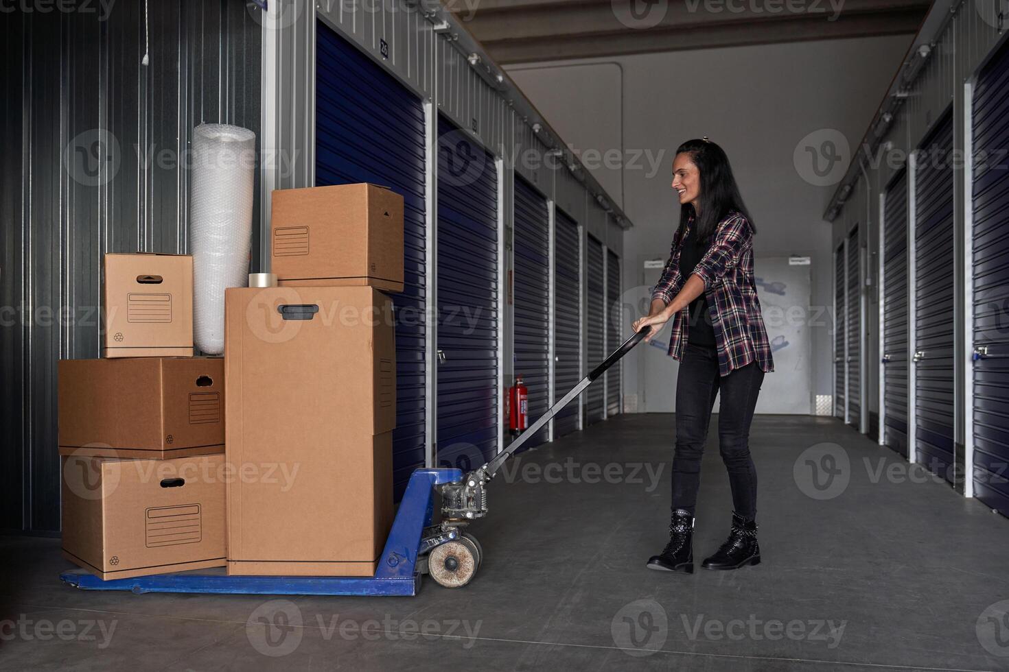 Content woman using pallet truck with packing boxes photo