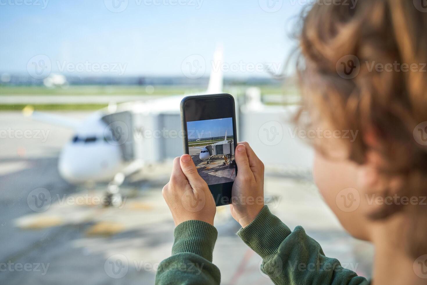 Crop kid photographing airplane on smartphone through window in photo