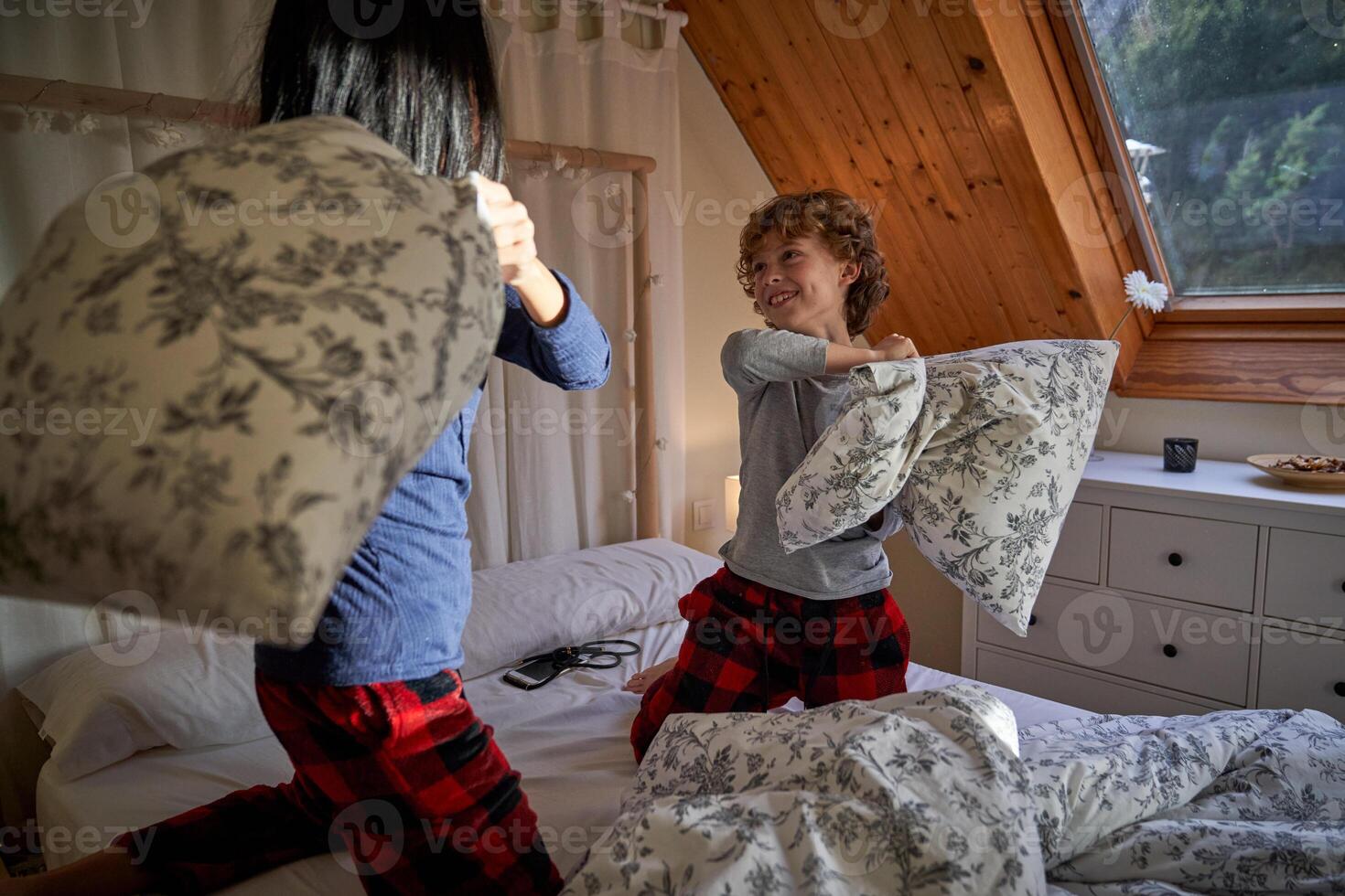 Mother and little son fighting with soft pillows on bed photo