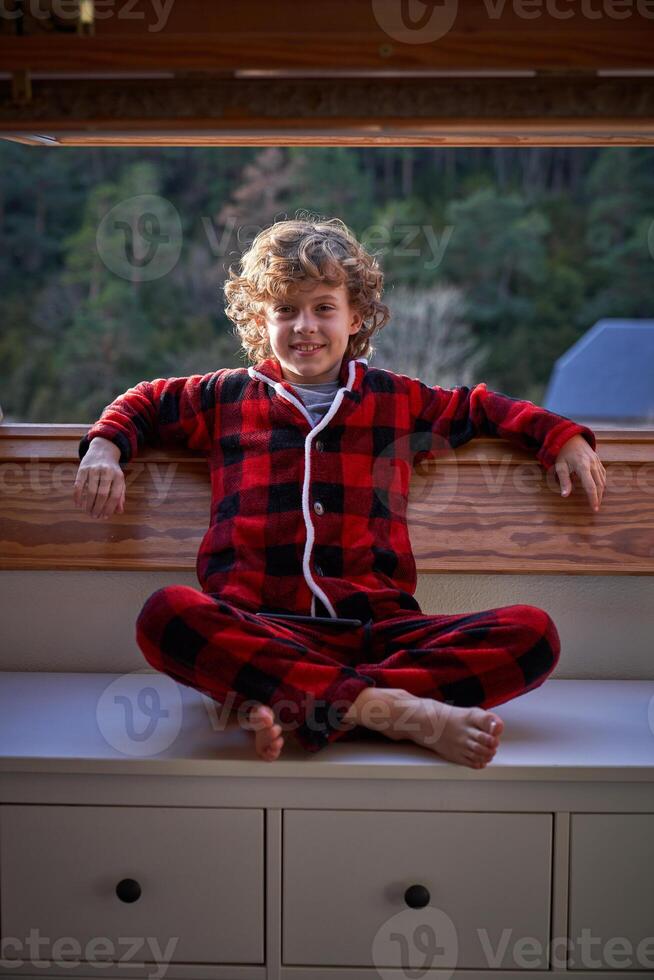 Positive boy sitting on cabinet near window in apartment photo