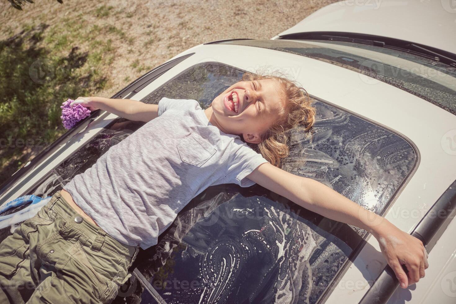 Joyful boy lying on white car window while resting after washing photo