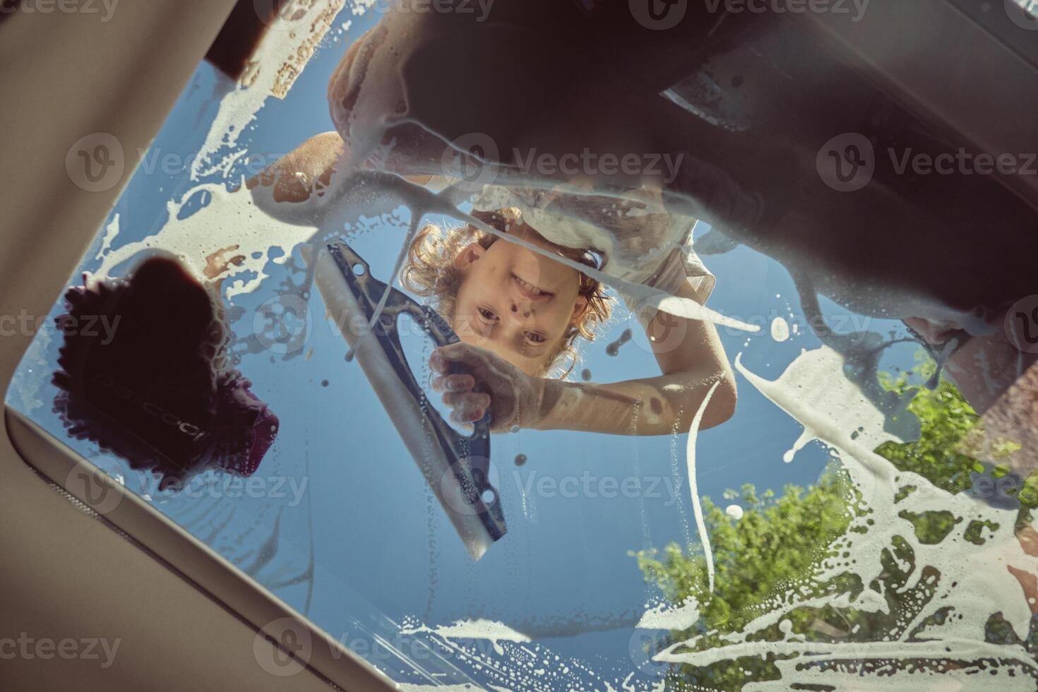 Cute boy using glass washing tool and cleaning car window photo