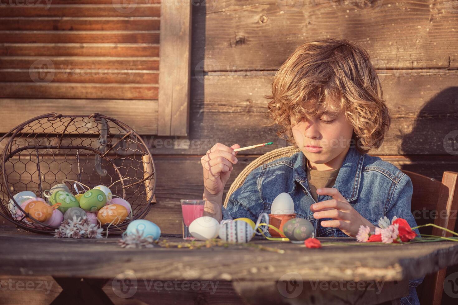Little boy painting Easter eggs with brush photo