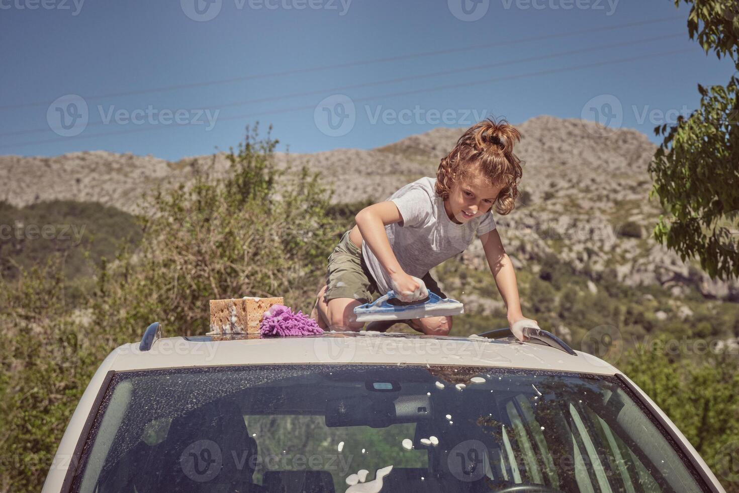 Boy washing car with window cleaning tool photo