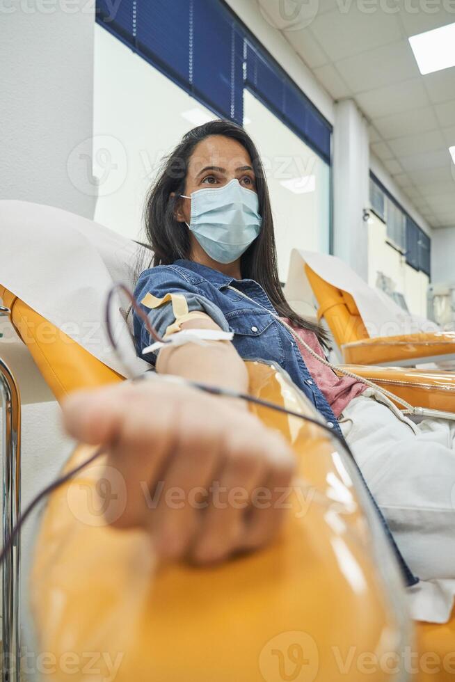 Woman in blue mask donating blood in donation center photo