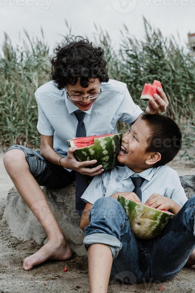 Teen boys playing while eating watermelon on beach photo