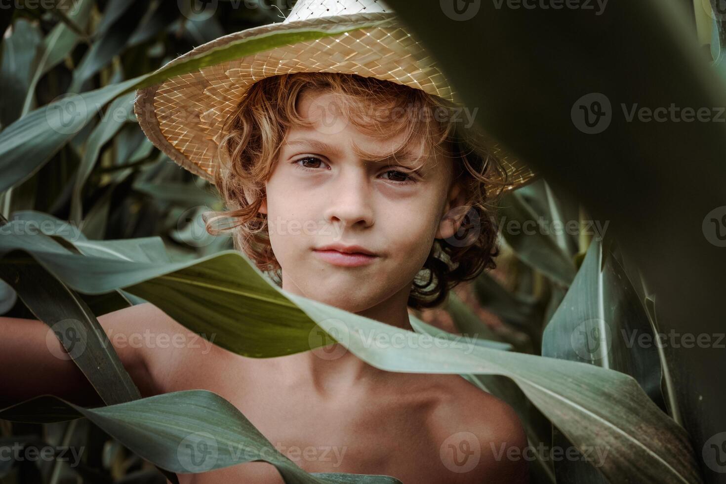 Charming boy in straw hat among green leaves photo