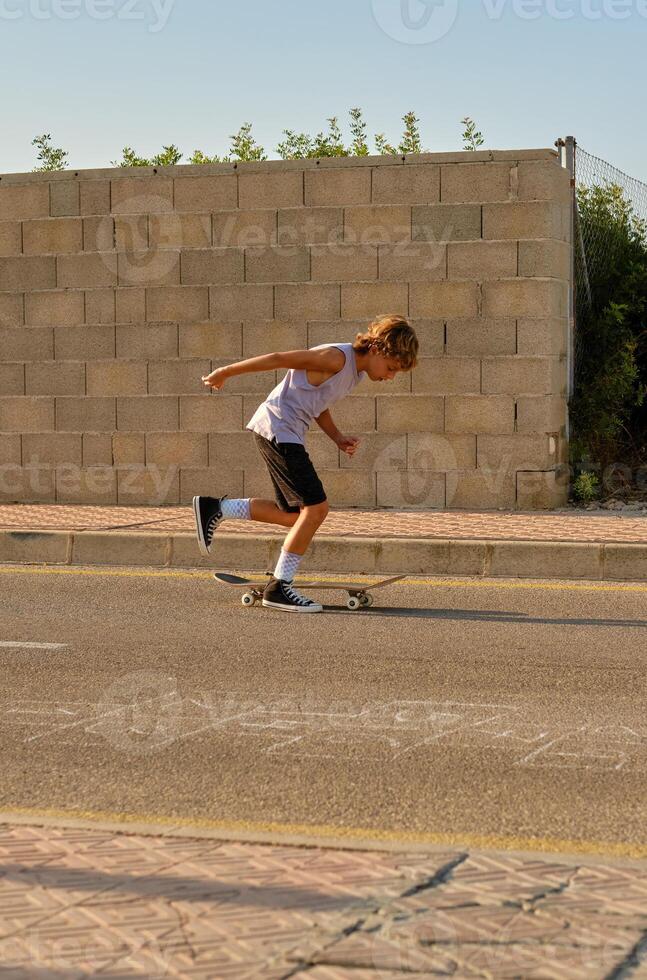 Active boy riding skateboard along roadway photo