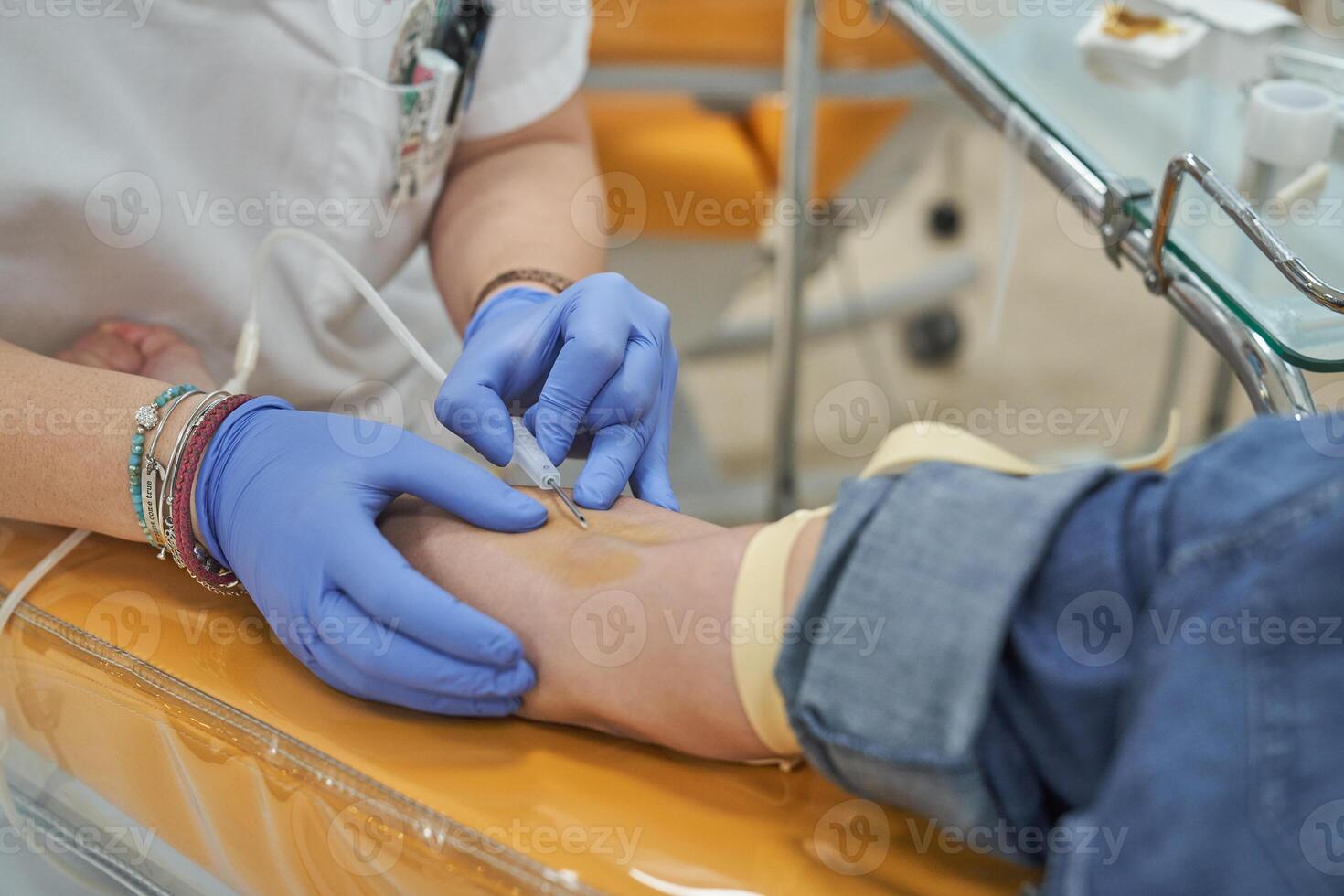 Crop female nurse making injection during blood donation in clin photo