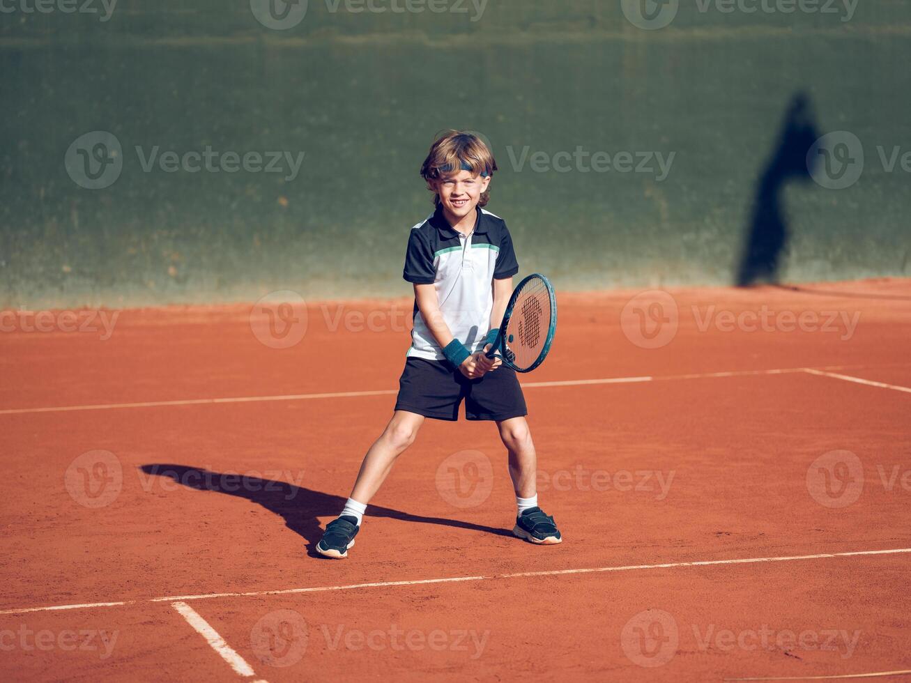 Happy child smiling while practicing tennis on clay court photo