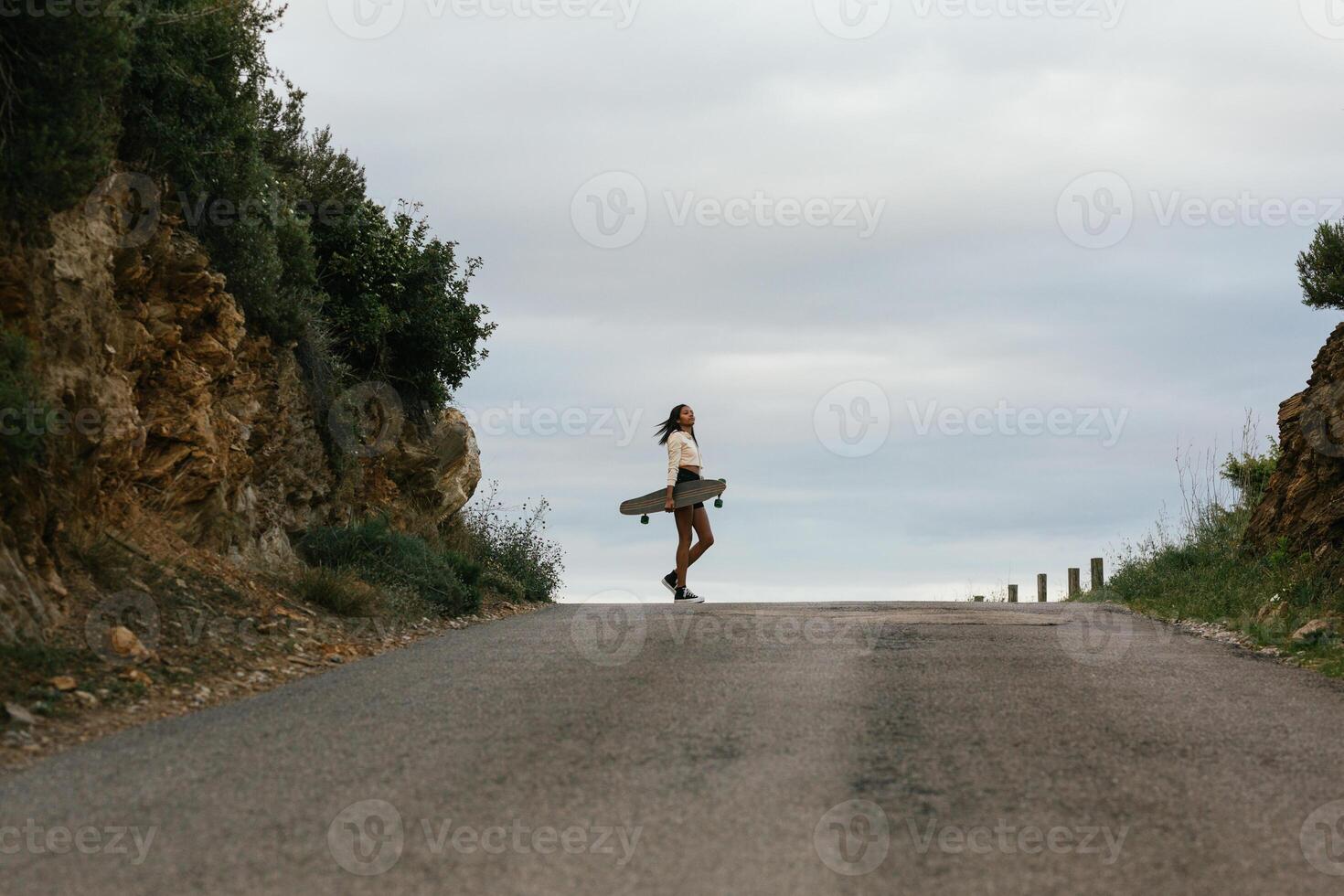 Pensive ethnic woman standing with longboard photo