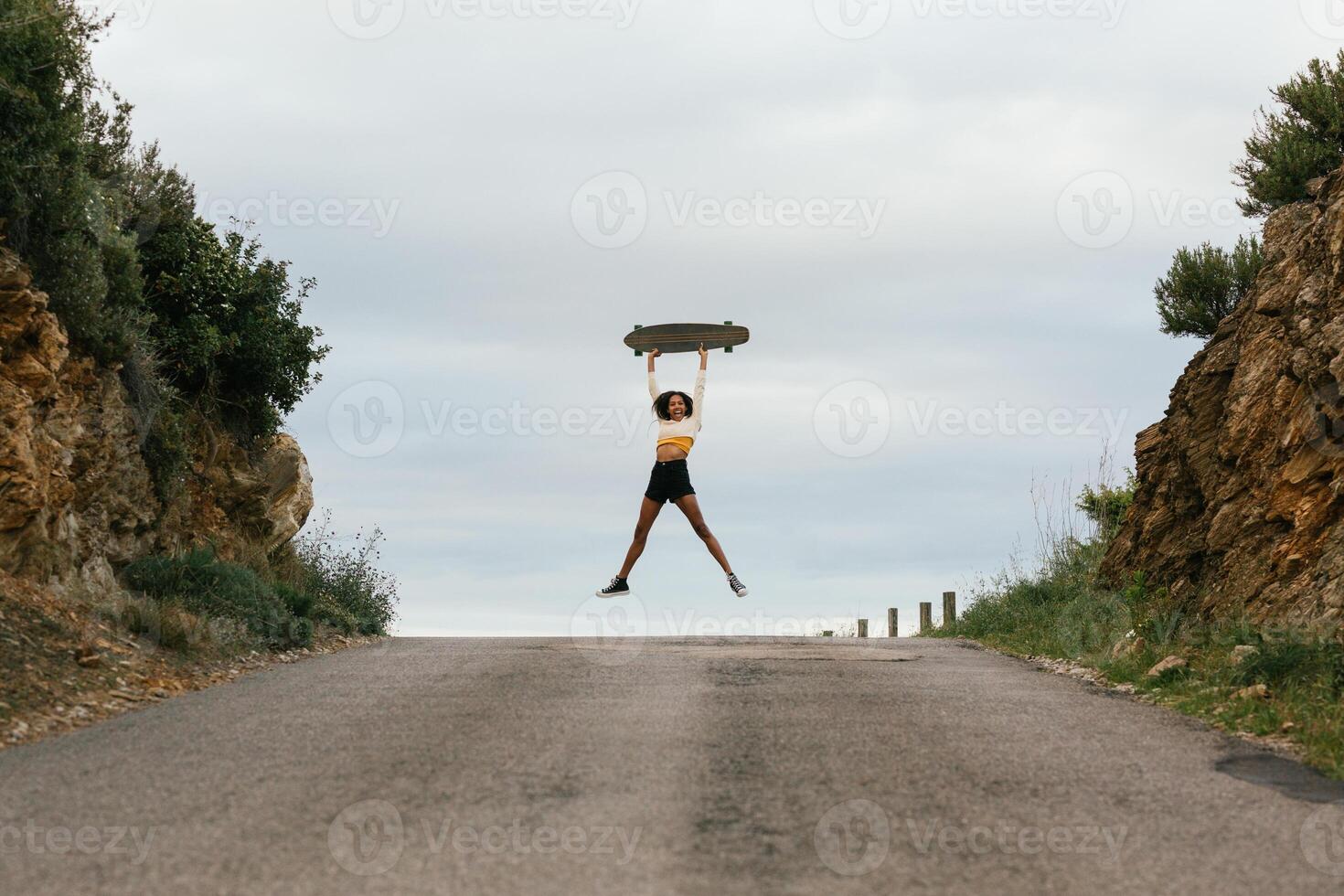 Joyful ethnic woman jumping high with longboard photo