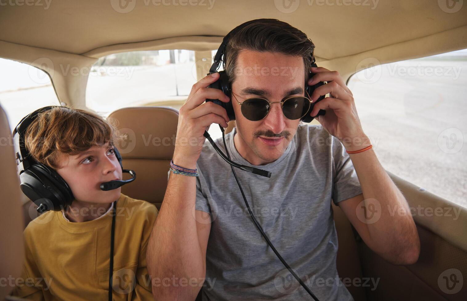 Young man with kid sitting in plane cabin and wearing headphones photo