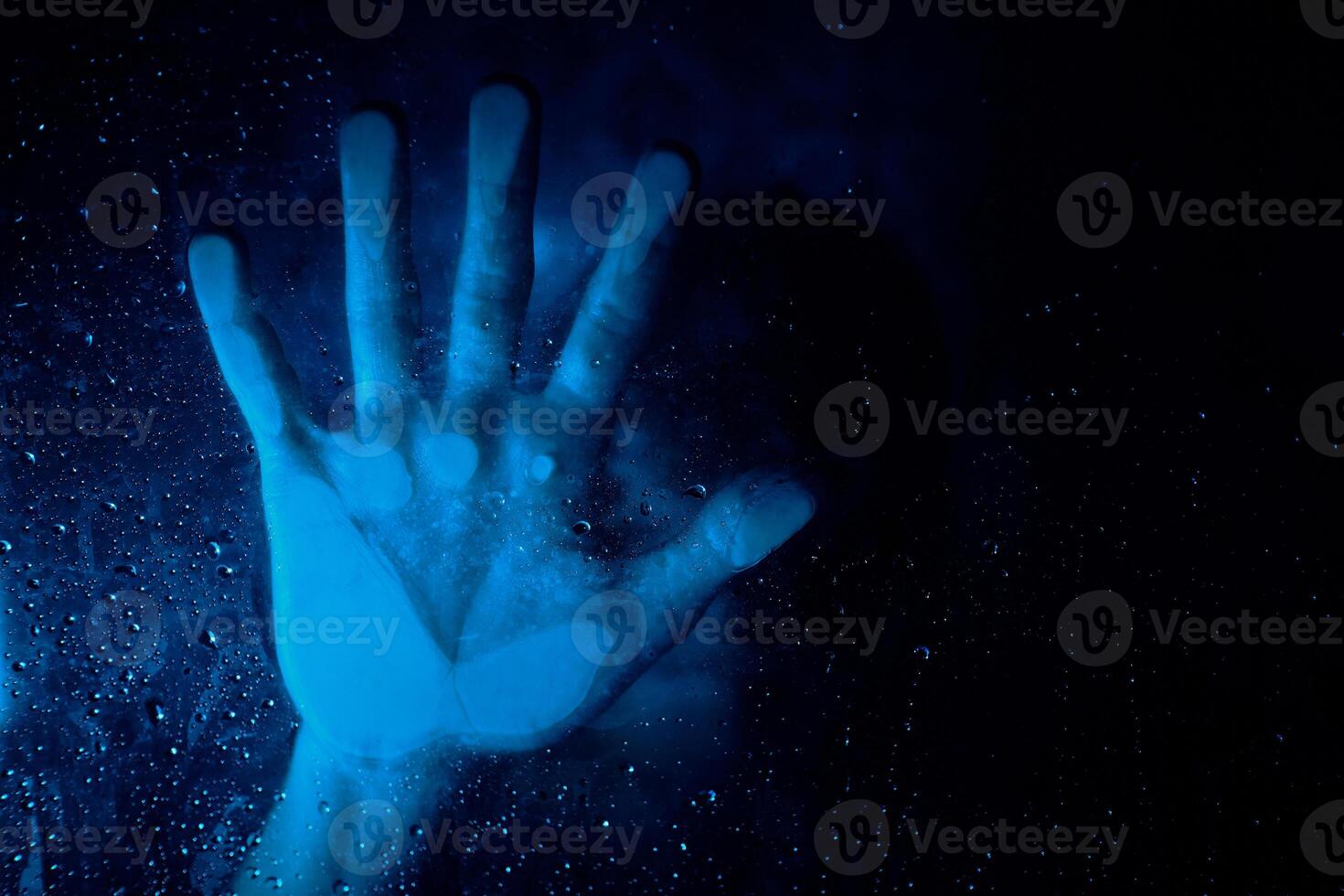 Anonymous hopeless person behind wet glass wall in neon light photo