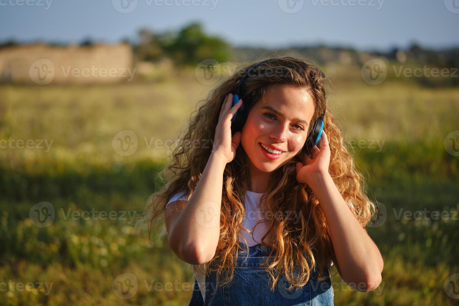 Cheerful woman listening to music in headphones in countryside photo