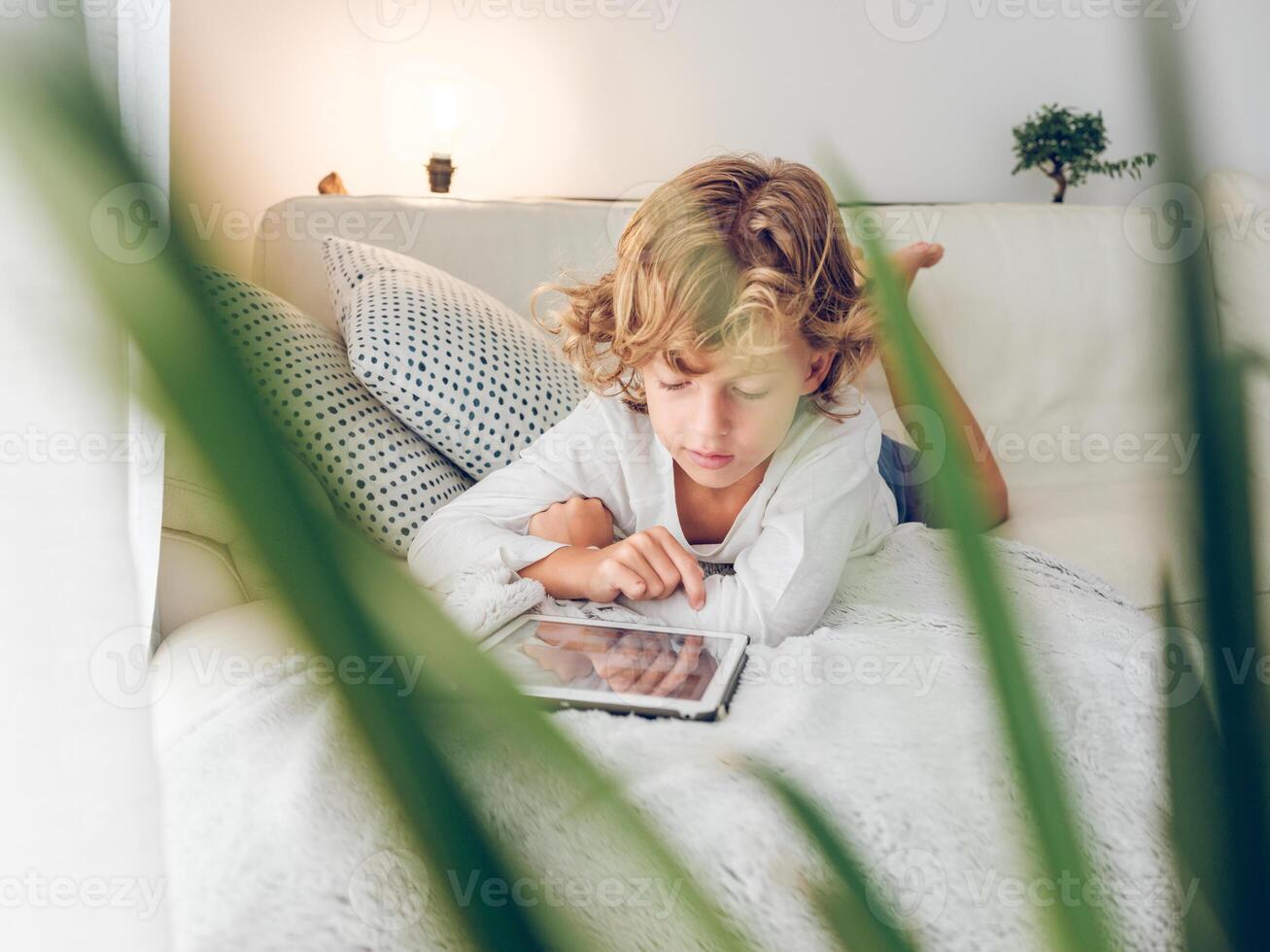 Focused preteen boy lying on sofa and browsing tablet photo