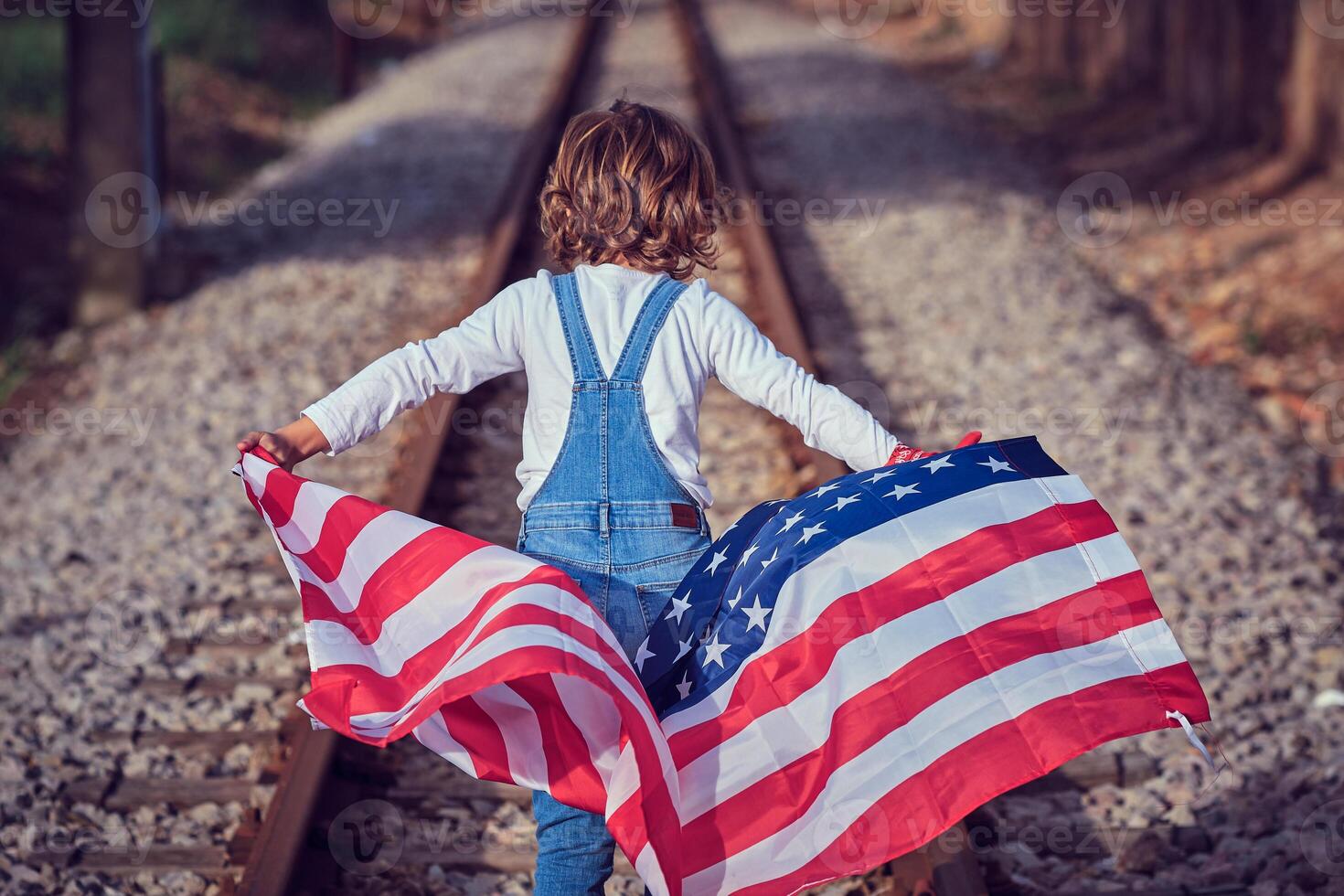 Kid holding USA flag while walking on rails photo