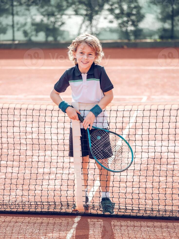 Smiling kid standing near net on court after playing tennis photo