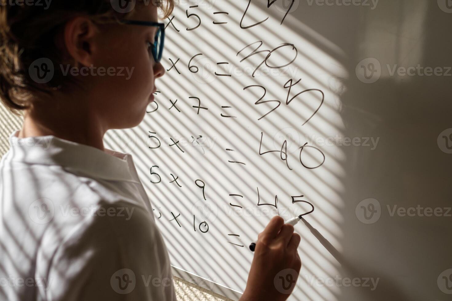 Diligent schoolboy near whiteboard during math lesson photo